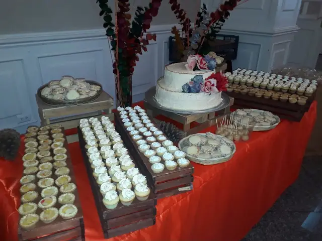 Mesa de postres con pastel de dos pisos, cupcakes y tartaletas